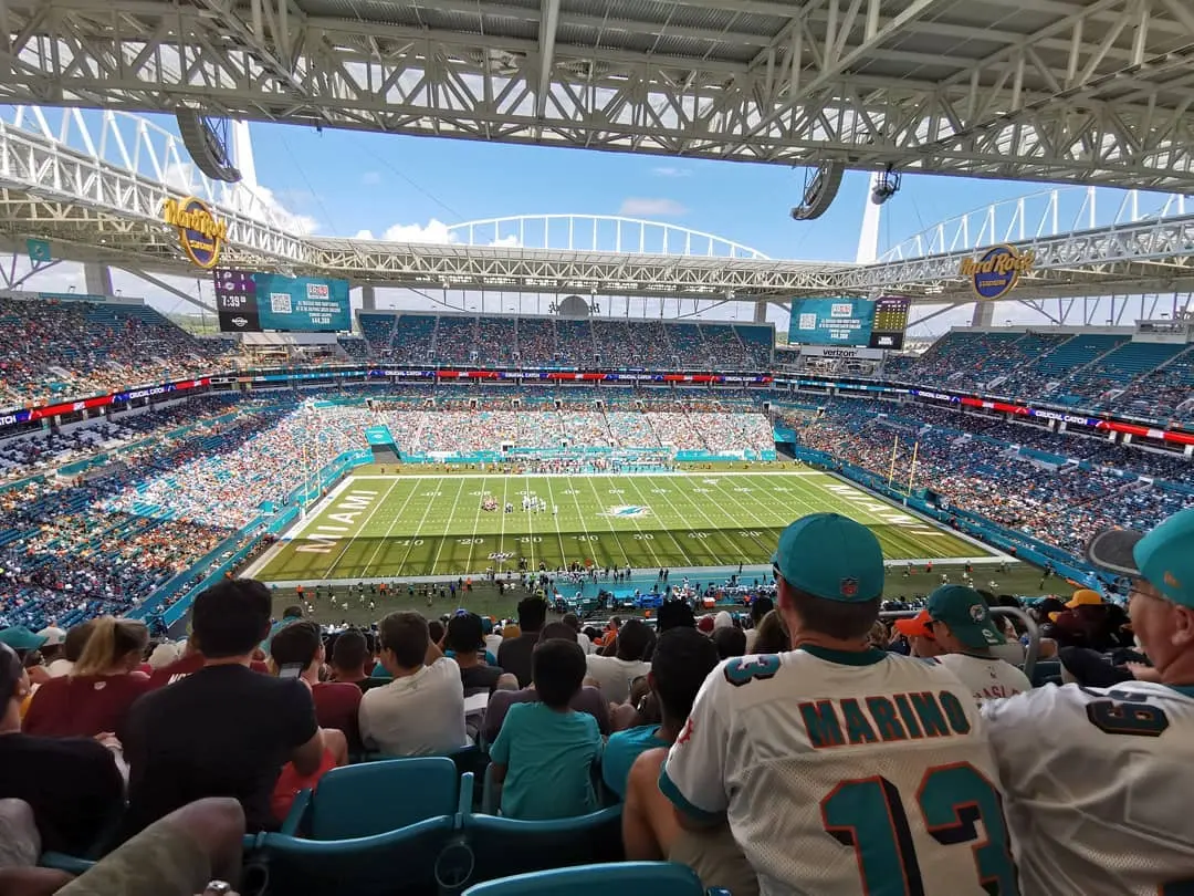 Fans in the stands watching a football game on a hot, bright day